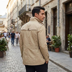 Man in khaki trench coat walking on a cobblestone street, back view