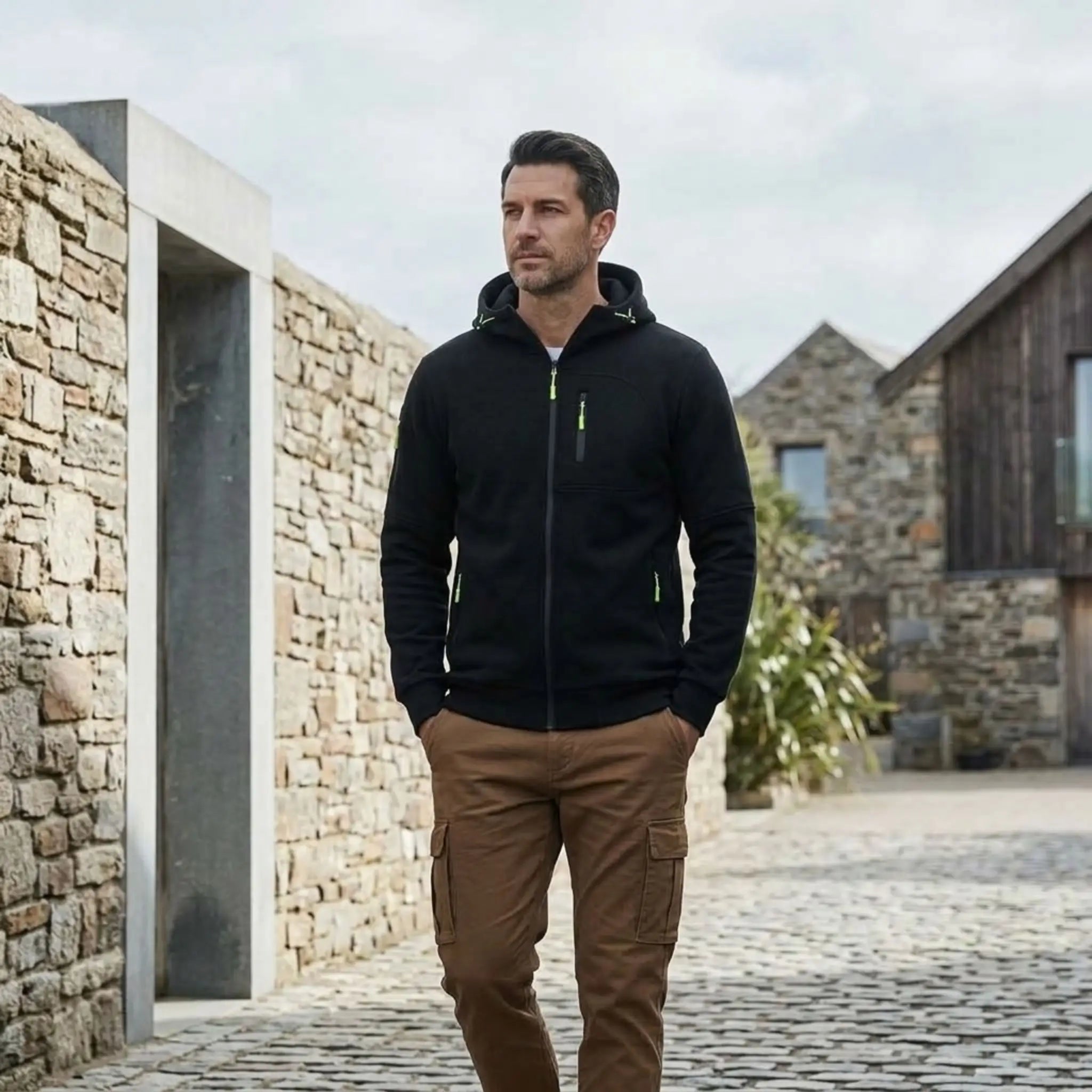 MannerCo black fleece hoodie styled with brown chinos beside stone buildings