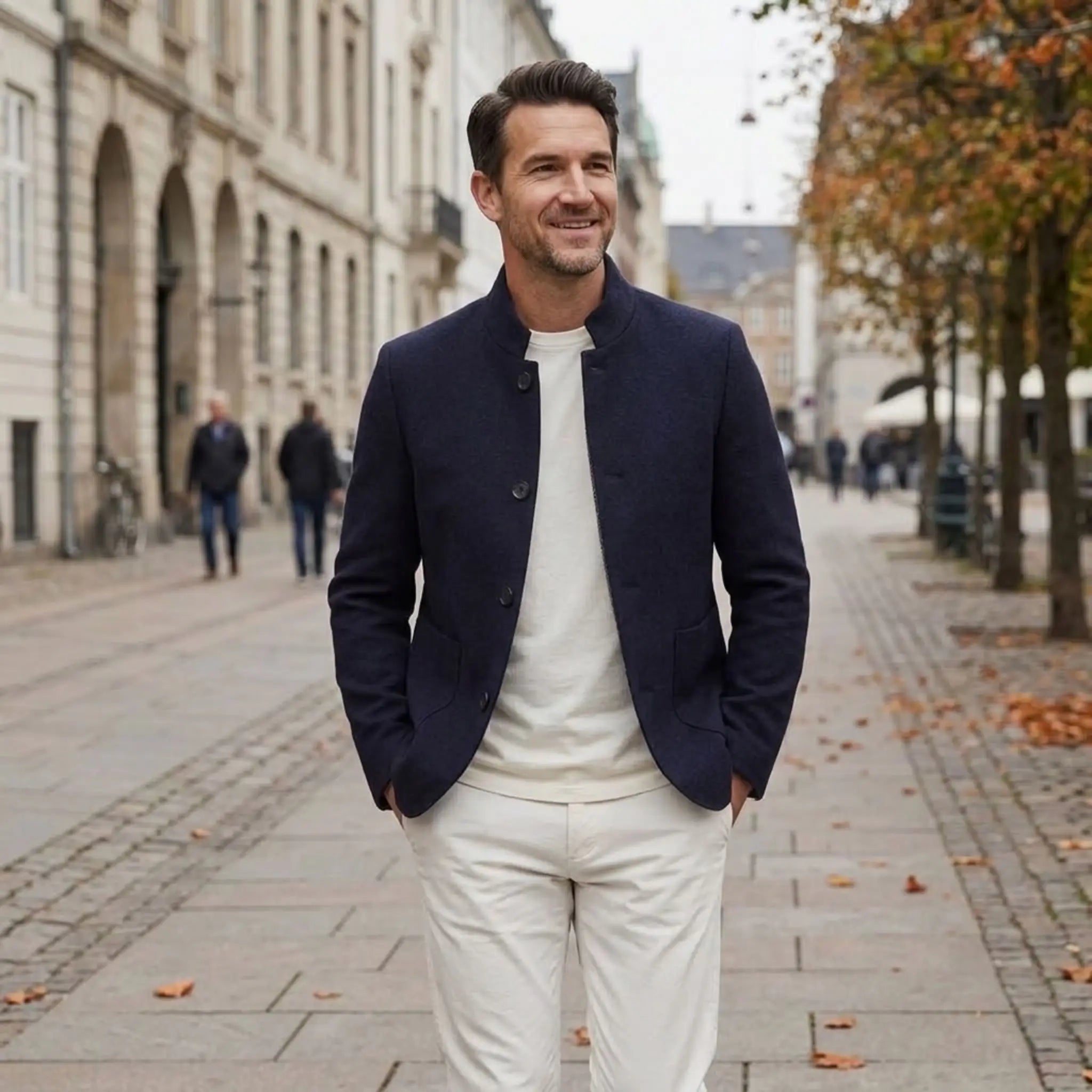 MannerCo navy blue wool overcoat with stand collar worn by man walking on European cobblestone street