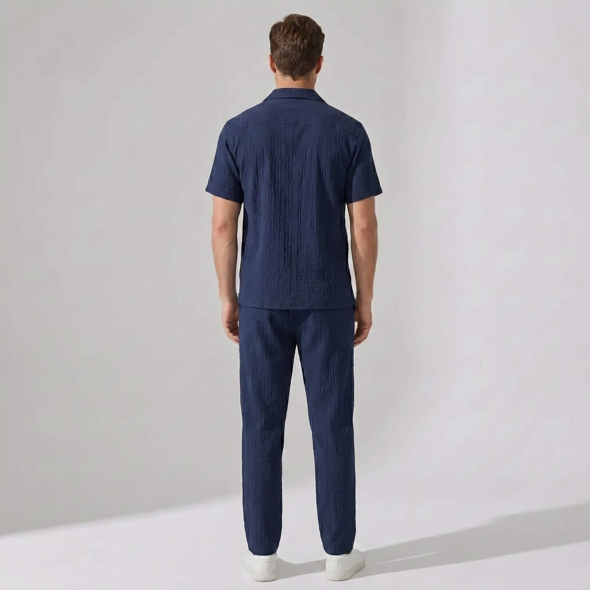 Back view of man wearing navy crinkled textured button up shirt and straight leg pants