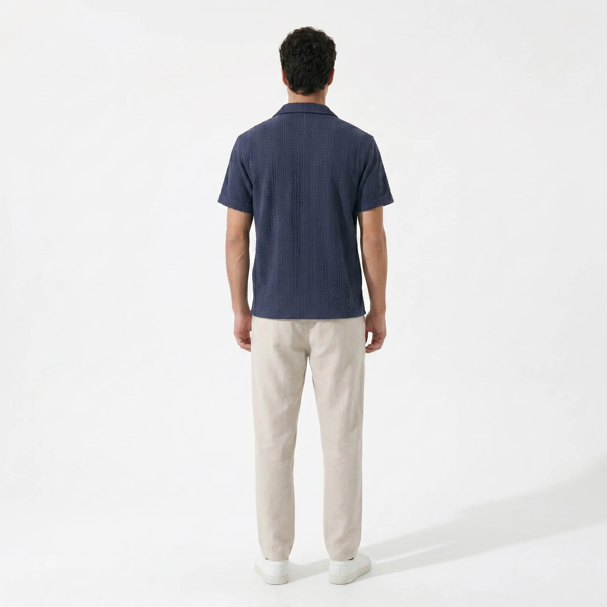 Back view of man wearing navy geometric jacquard button up shirt and straight leg linen pants
