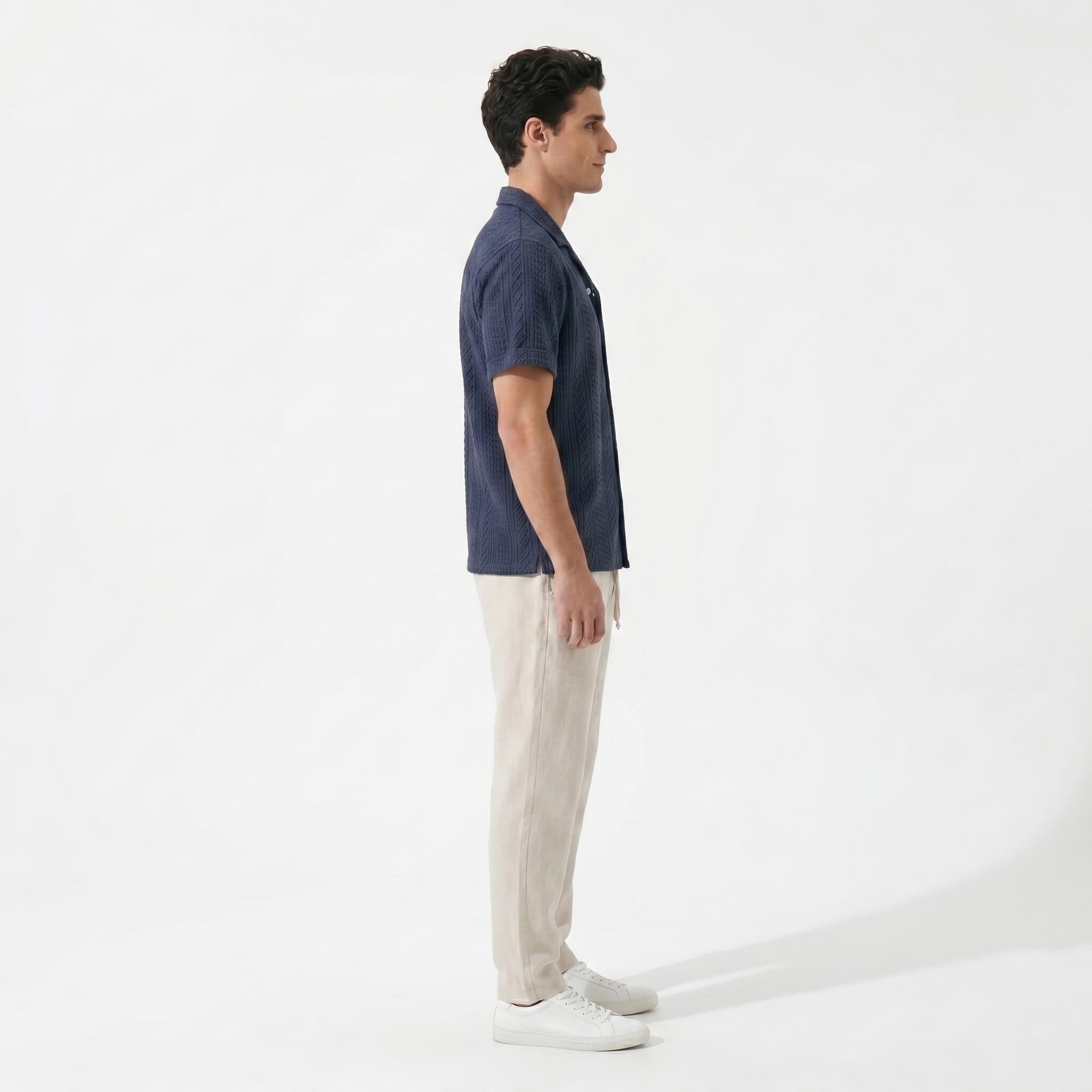 Side view of man in navy geometric jacquard button up shirt and straight leg linen pants on plain background