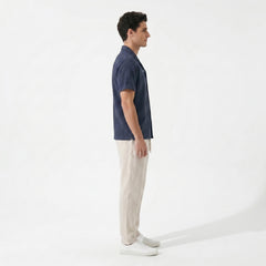 Side view of man in navy geometric jacquard button up shirt and straight leg linen pants on plain background