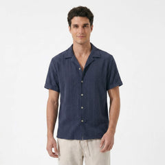 Three quarter view of man in navy geometric jacquard shirt and linen pants on white background