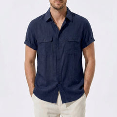 Three quarter view of man in navy linen rayon blend utility shirt and linen pants on plain background