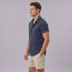 Side view of man in navy striped cotton blend button up shirt and crinkle textured drawstring shorts