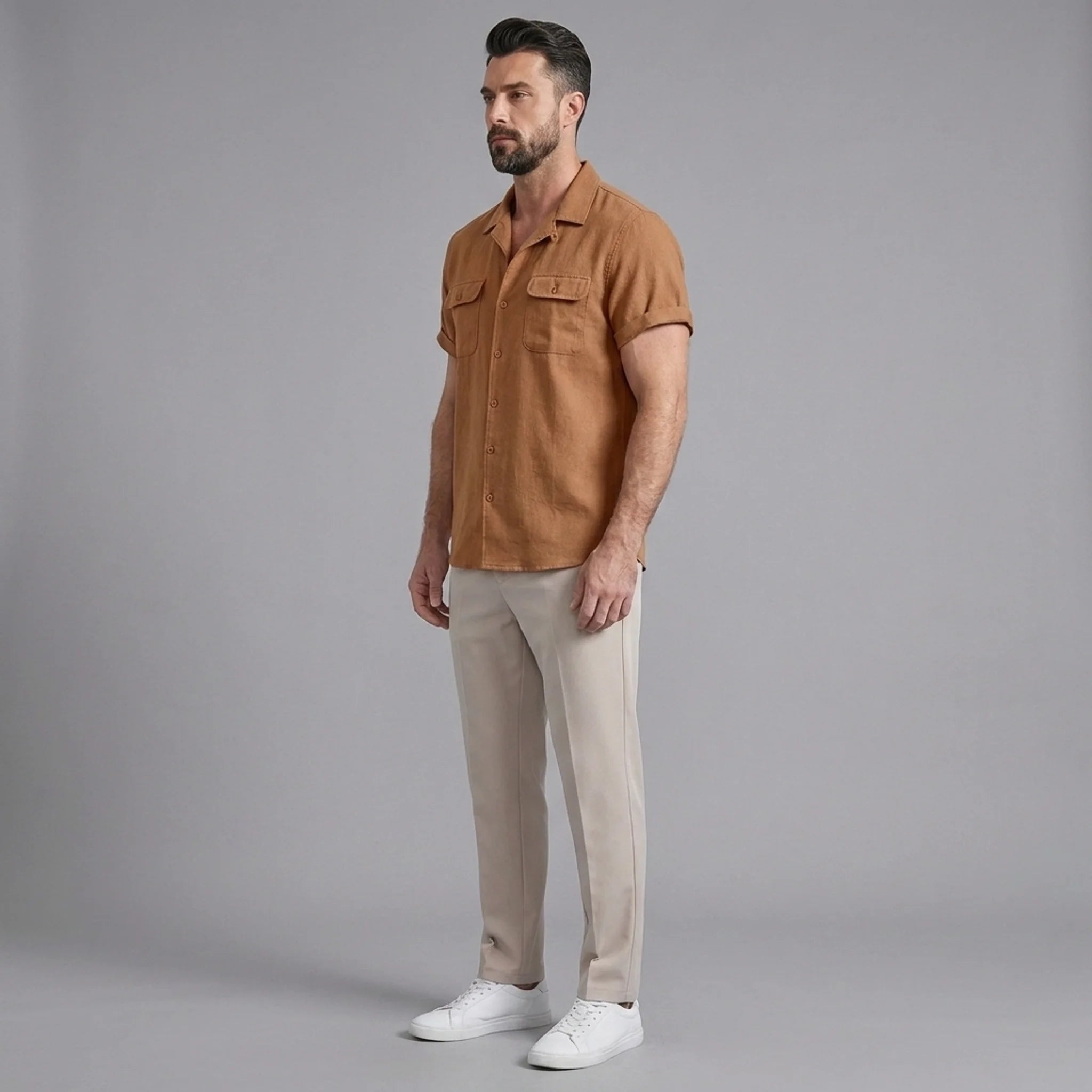 Side view of man in orange linen Cuban collar shirt and slim fit tapered trousers on plain background