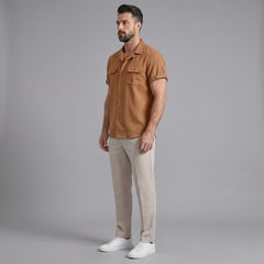 Side view of man in orange linen Cuban collar shirt and slim fit tapered trousers on plain background