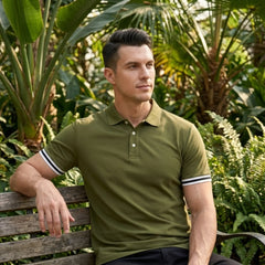Man in military green polo with striped cuffs seated on bench in lush garden setting