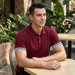 Man wearing wine red polo shirt with striped cuffs sitting at outdoor cafe table