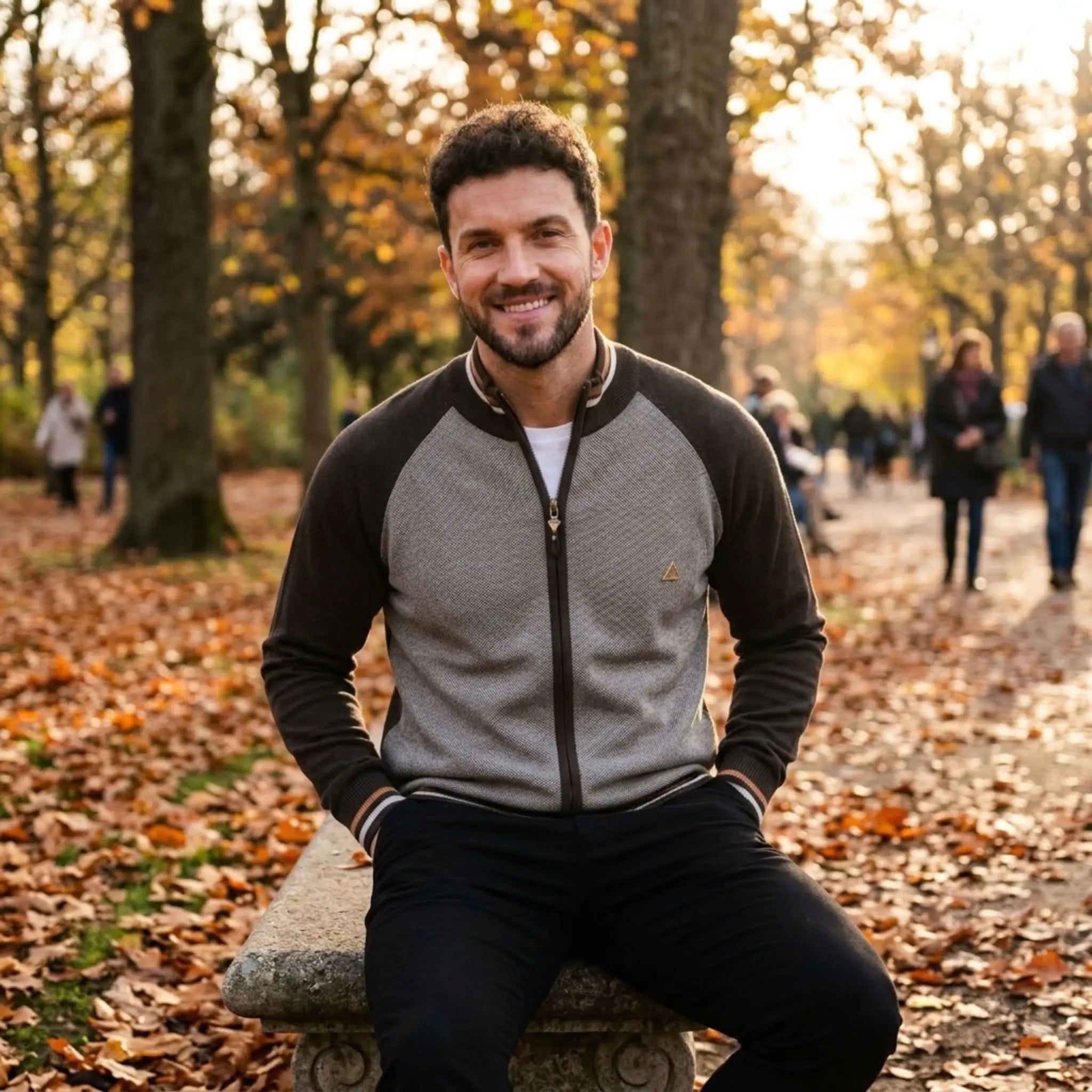 MannerCo brown raglan sleeve cardigan worn by man sitting on stone bench in autumn park