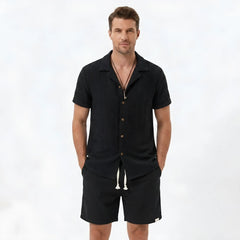 Back view of man wearing tan floral checkerboard jacquard Cuban shirt and linen drawstring shorts