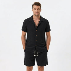 Back view of man wearing tan floral checkerboard jacquard Cuban shirt and linen drawstring shorts