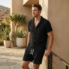Man in tan floral checkerboard jacquard Cuban shirt and linen drawstring shorts in sunny outdoor scene