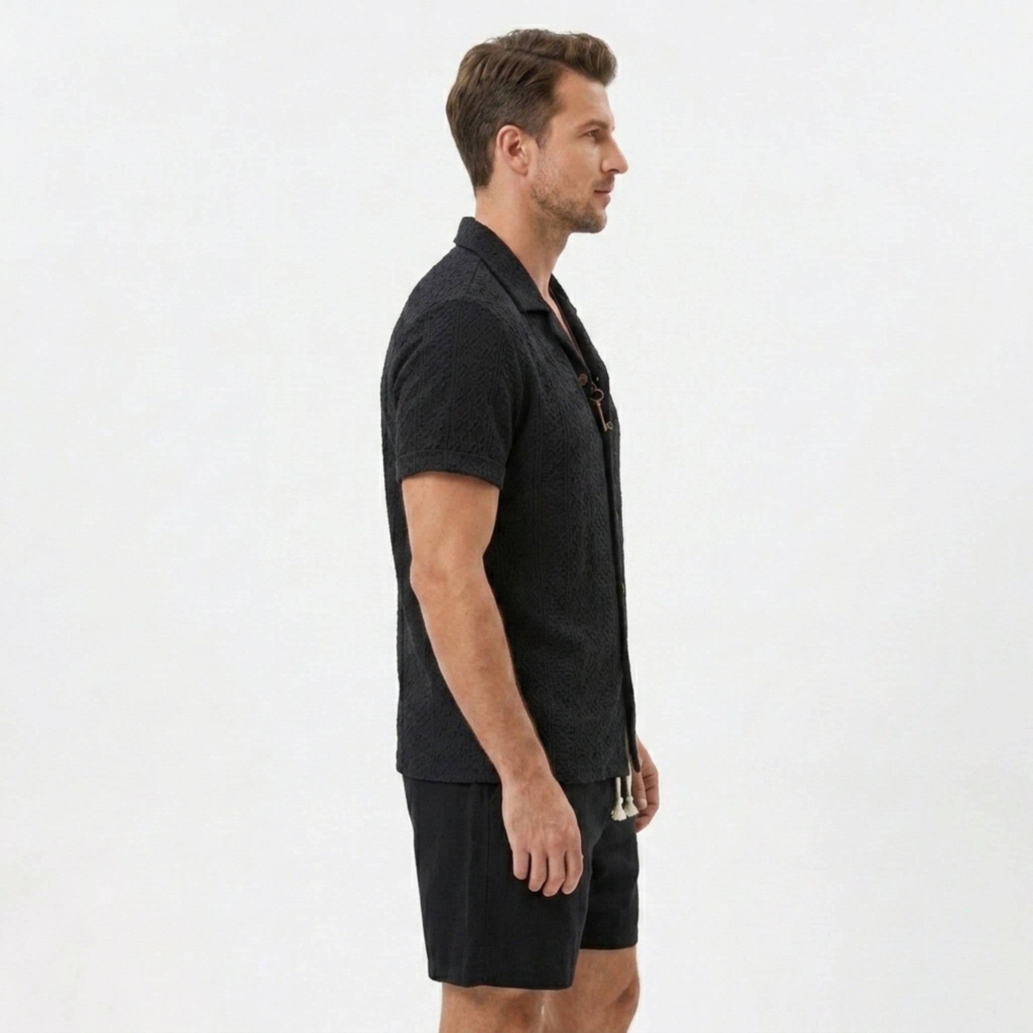 Side view of man in tan floral checkerboard jacquard Cuban shirt and linen drawstring shorts