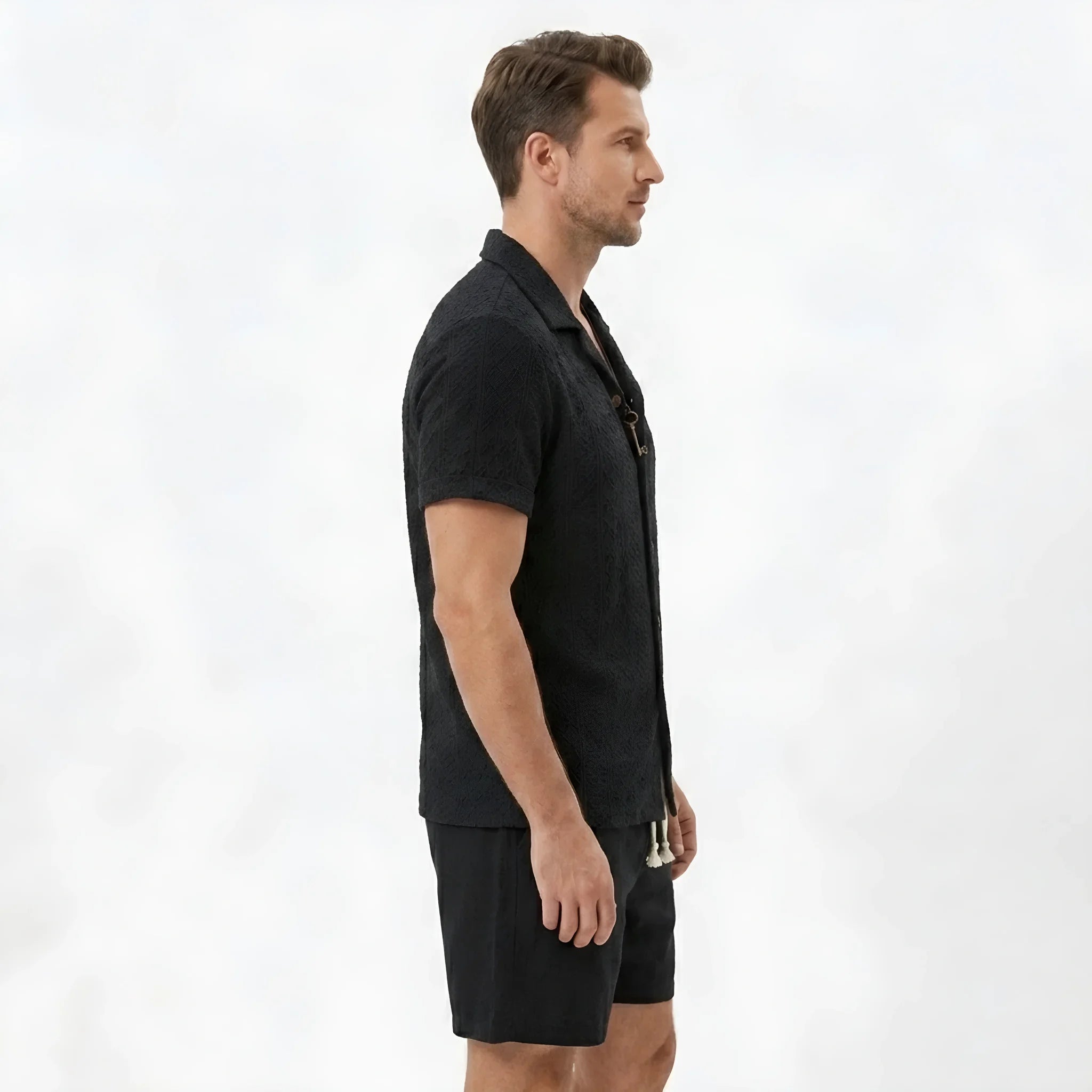 Side view of man in tan floral checkerboard jacquard Cuban shirt and linen drawstring shorts