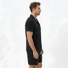 Side view of man in tan floral checkerboard jacquard Cuban shirt and linen drawstring shorts