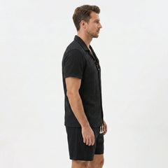 Side view of man in tan floral checkerboard jacquard Cuban shirt and linen drawstring shorts