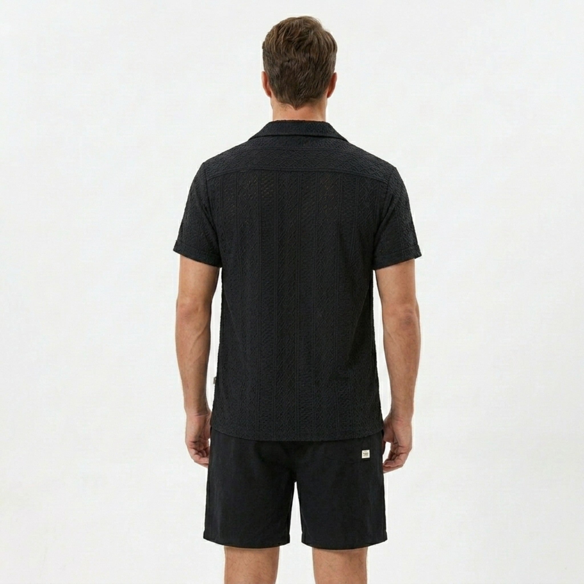 Three quarter view of man in tan floral checkerboard jacquard Cuban shirt and drawstring shorts