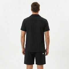 Three quarter view of man in tan floral checkerboard jacquard Cuban shirt and drawstring shorts