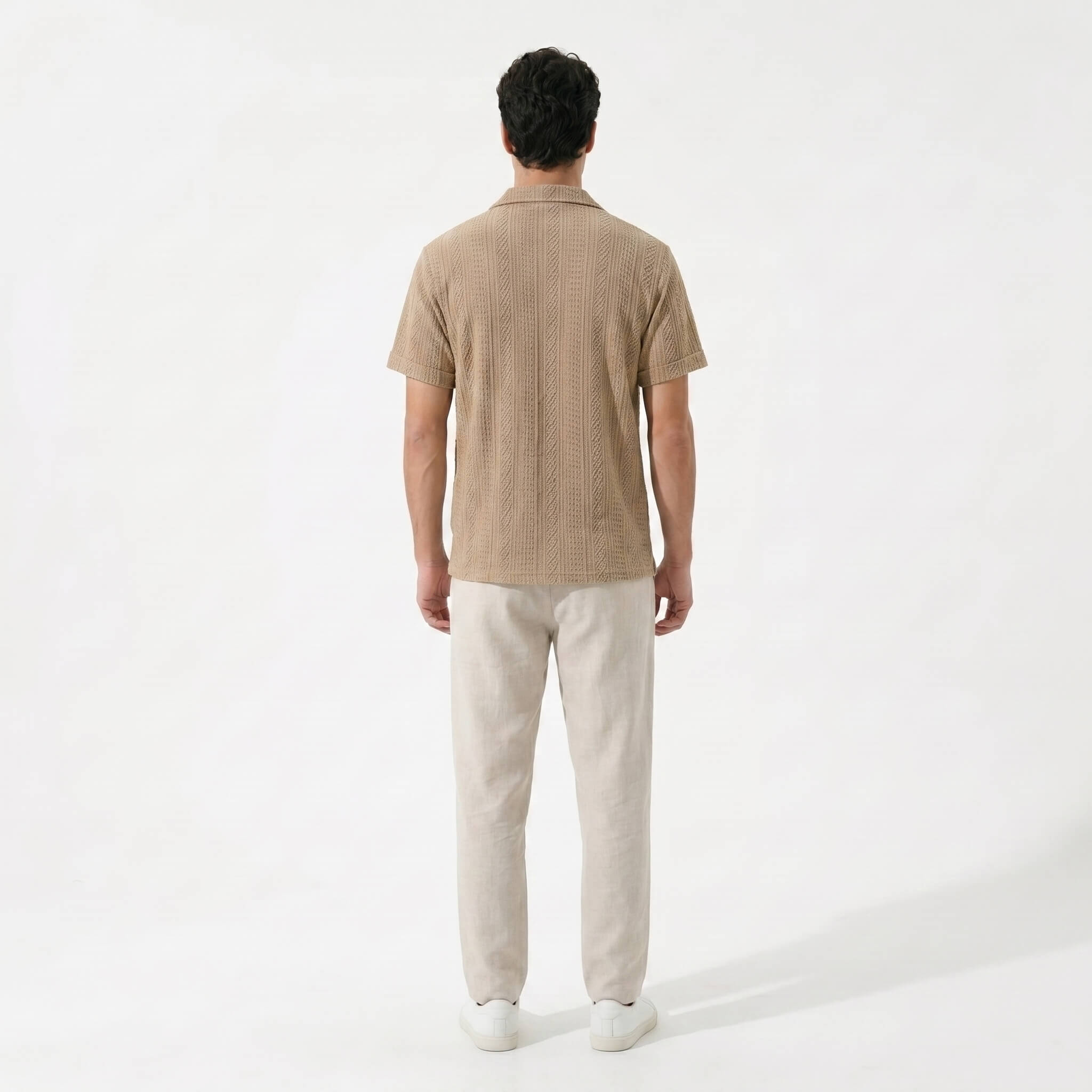 Side view of man wearing tan geometric jacquard button up shirt and linen pants outdoors