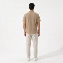 Side view of man wearing tan geometric jacquard button up shirt and linen pants outdoors