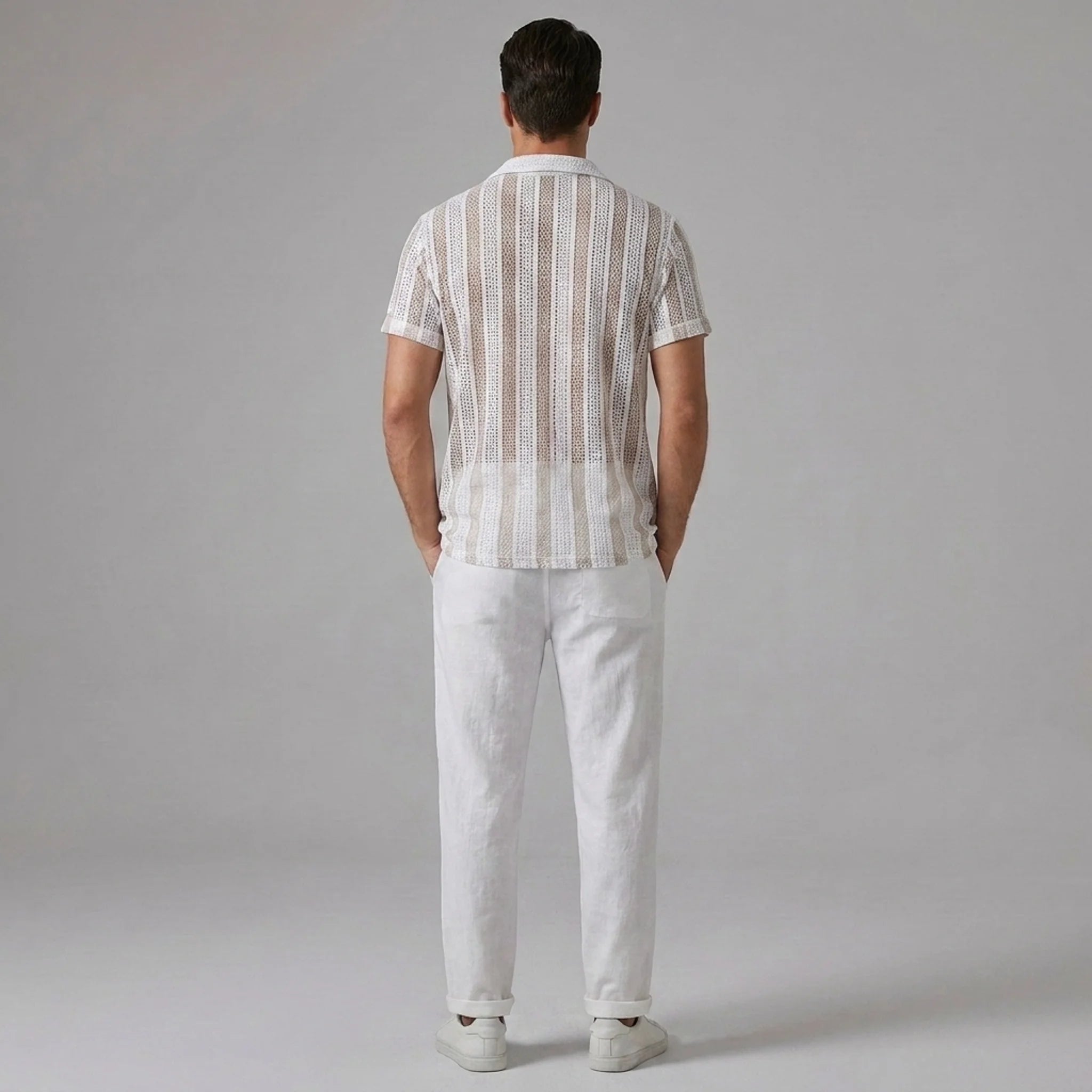Side view of man wearing tan striped mesh Cuban shirt and beige linen pants on light background
