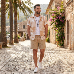 Man in tan tribal geometric patchwork shirt and swim shorts walking in sunny outdoor beach scene