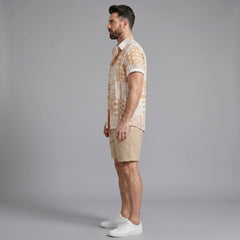 Side view of man in tan tribal geometric patchwork button up shirt and swim shorts