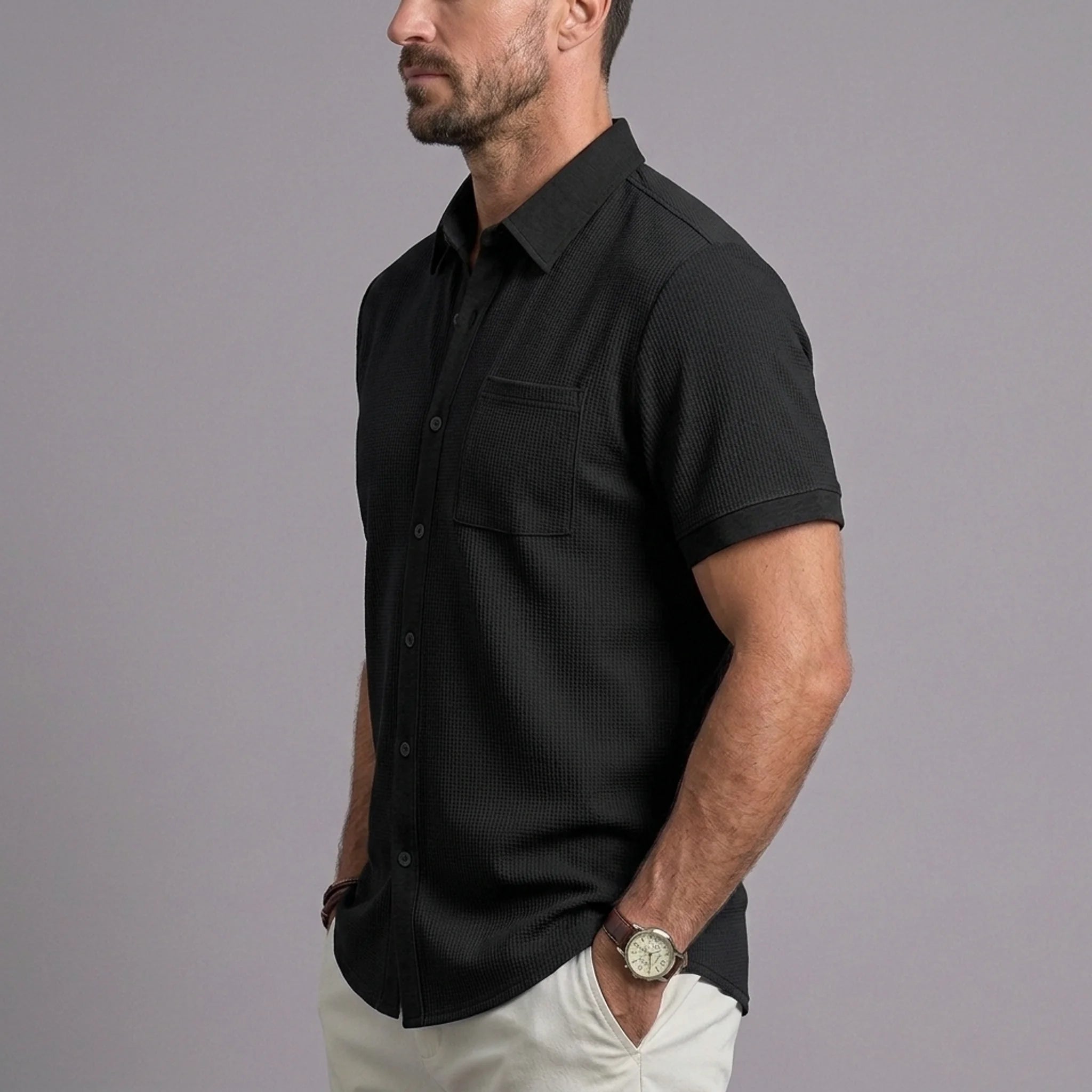 Man wearing black waffle knit short sleeve shirt with chest pocket and white chinos, side view