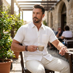 Man in white waffle knit polo shirt seated at sunny outdoor cafe, relaxed smart-casual style