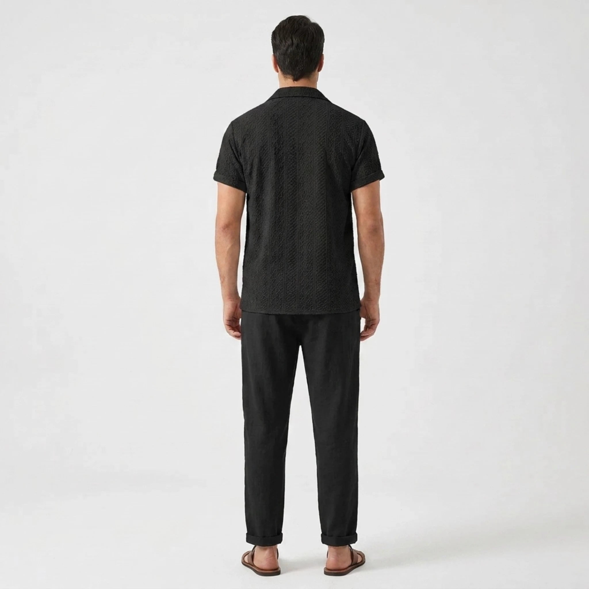 Back view of man in white floral checkerboard jacquard Cuban shirt and straight leg linen pants