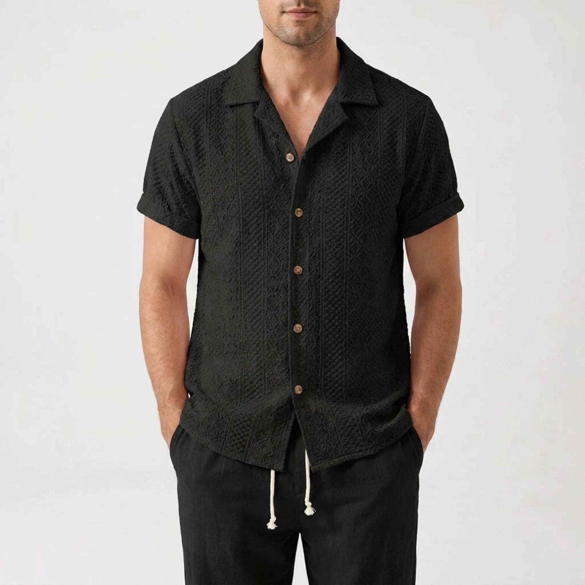 Man in white floral checkerboard jacquard Cuban shirt and linen pants walking in sunny outdoor setting