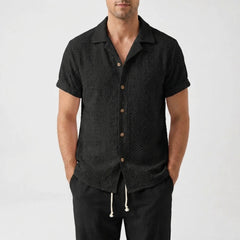 Man in white floral checkerboard jacquard Cuban shirt and linen pants walking in sunny outdoor setting