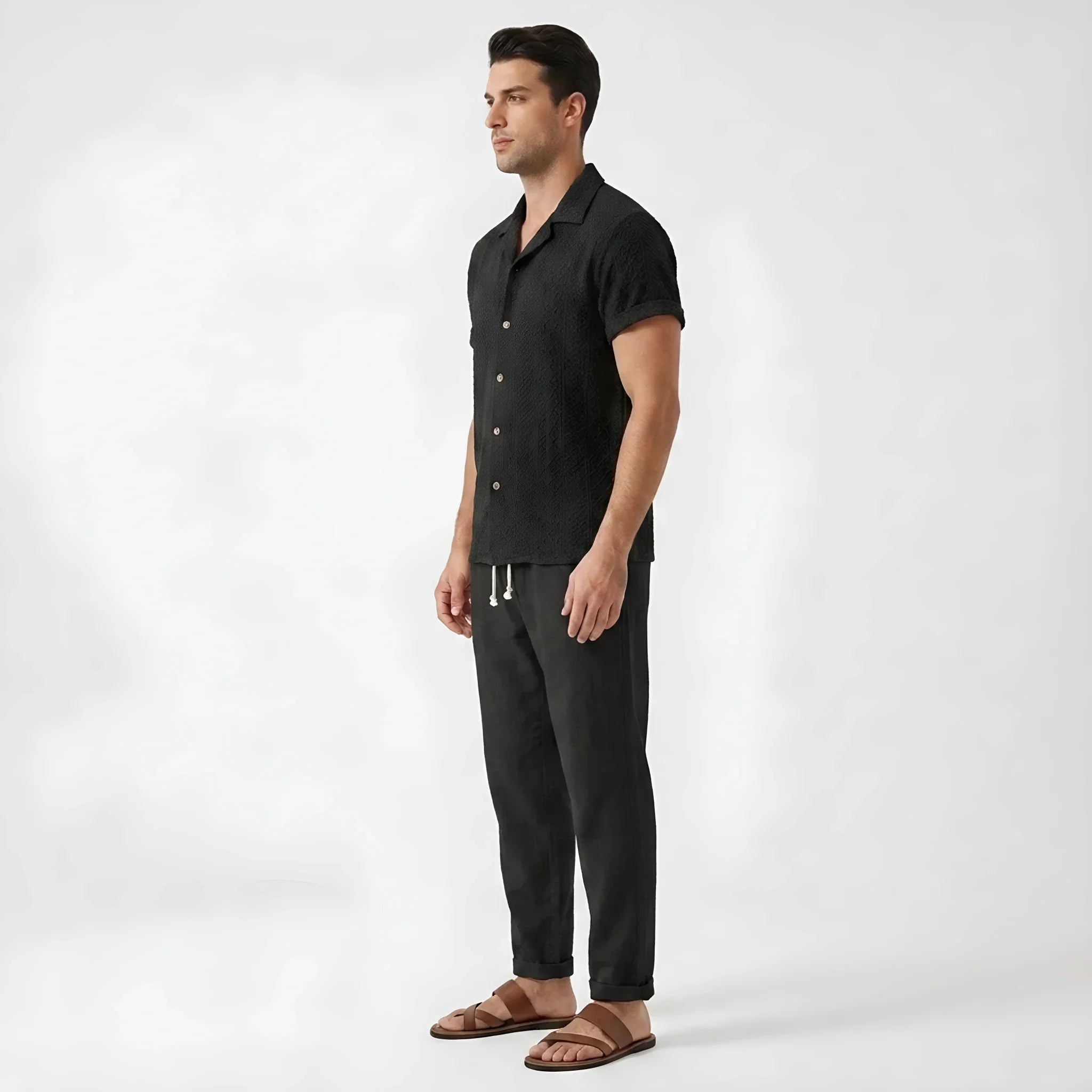 Three quarter view of man wearing white floral checkerboard jacquard Cuban shirt and linen pants