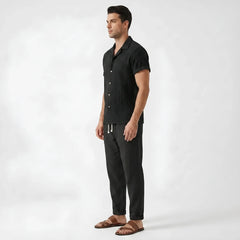 Three quarter view of man wearing white floral checkerboard jacquard Cuban shirt and linen pants