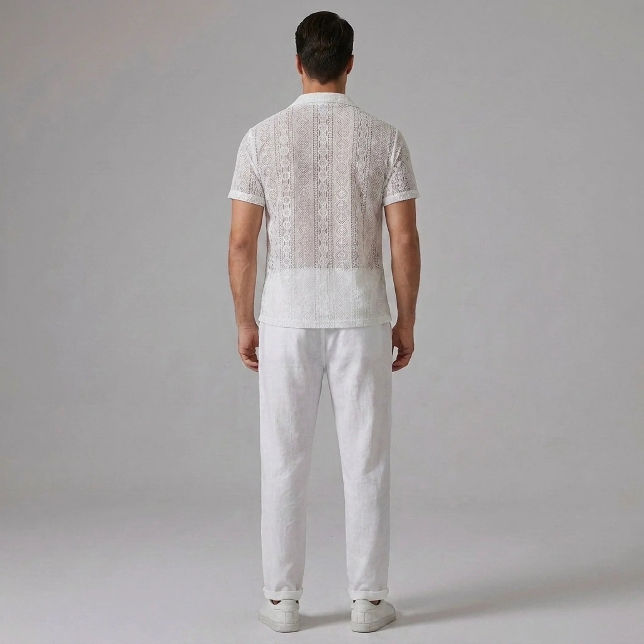 Three quarter view of man in white geometry textured Cuban shirt and linen pants on plain background