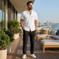 Man in white linen Cuban collar shirt and slim fit tapered trousers walking in sunny outdoor summer scene