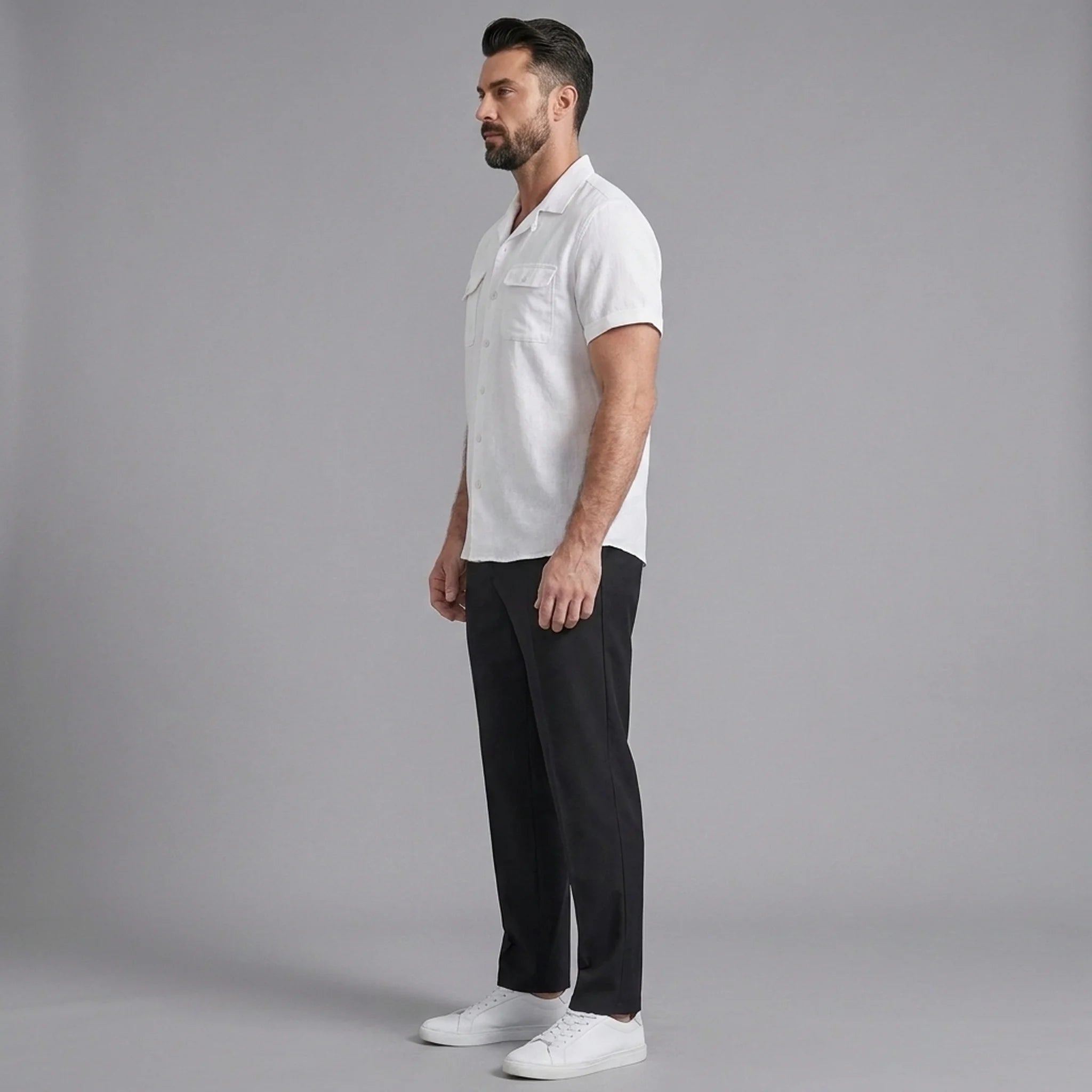 Side view of man in white linen Cuban collar shirt and slim fit tapered trousers on plain background