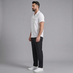 Side view of man in white linen Cuban collar shirt and slim fit tapered trousers on plain background