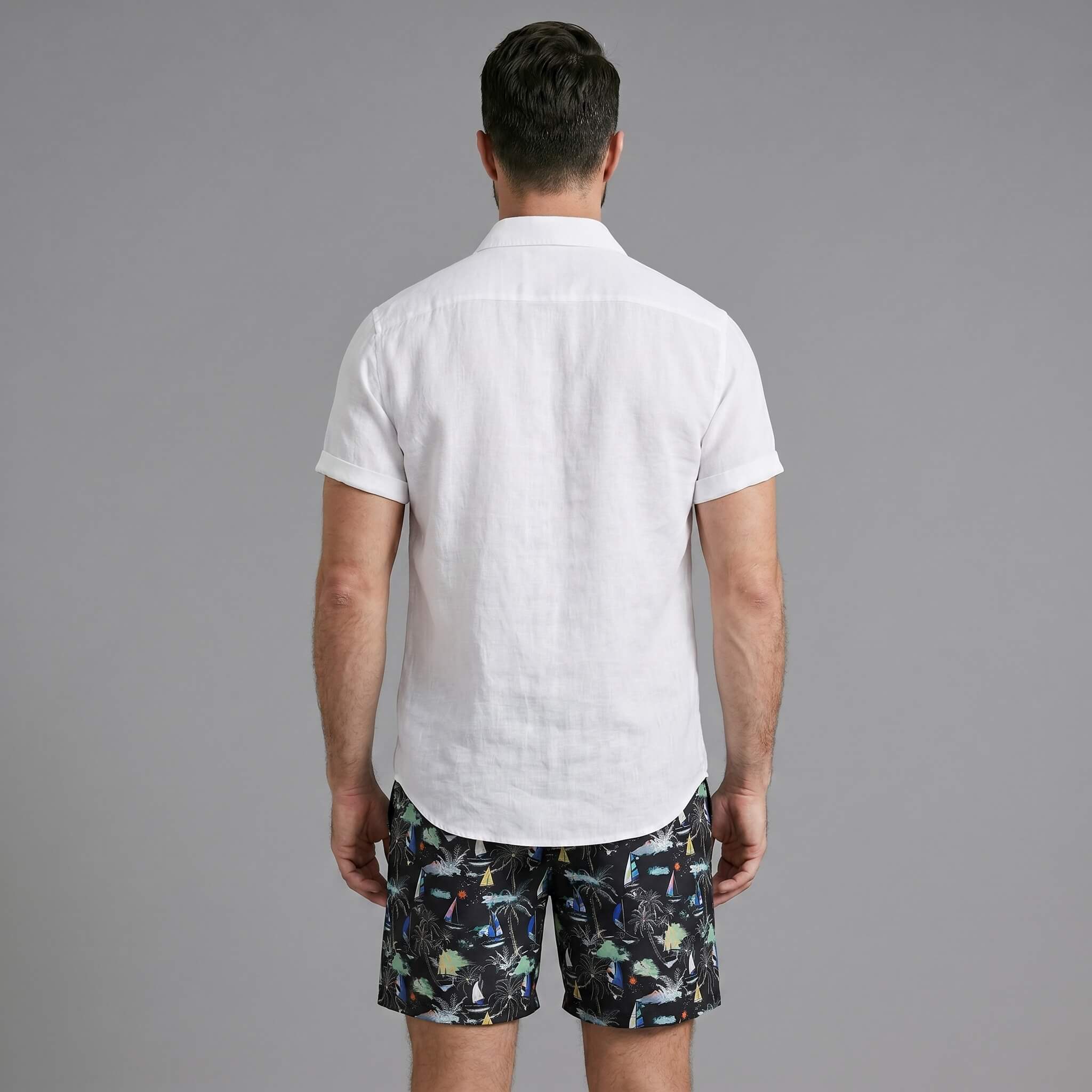 Back view of man wearing white linen rayon shirt and black palm tree print swim shorts