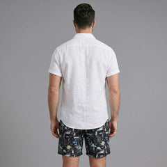 Back view of man wearing white linen rayon shirt and black palm tree print swim shorts