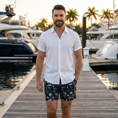 Man in white linen rayon shirt and black palm tree swim shorts in sunny outdoor beach scene