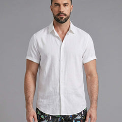 Three quarter view of man in white linen rayon shirt and black palm tree print swim shorts