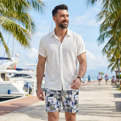 Man wearing white linen rayon shirt and white palm tree print swim shorts in outdoor lifestyle setting