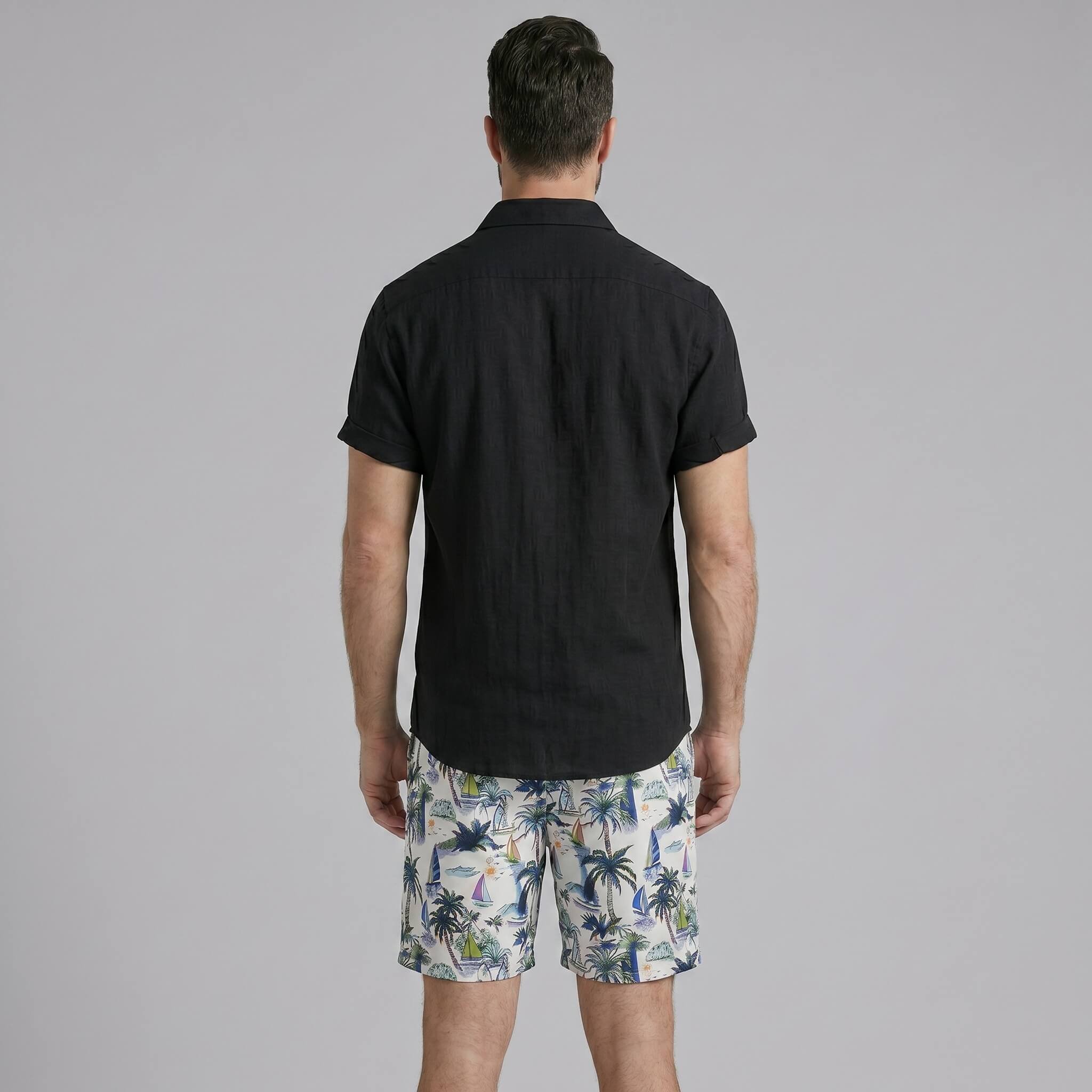 Side view of man in white linen rayon button up shirt and white palm tree print swim shorts