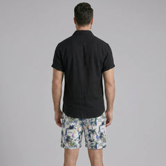 Side view of man in white linen rayon button up shirt and white palm tree print swim shorts