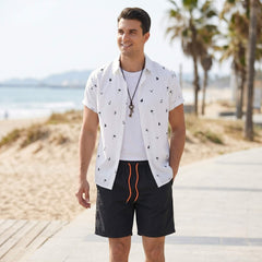 Man wearing white palm tree anchor sailboat print shirt and swim shorts in outdoor lifestyle setting