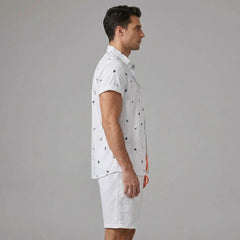 Side view of man in white palm tree anchor sailboat print shirt and swim shorts on plain background