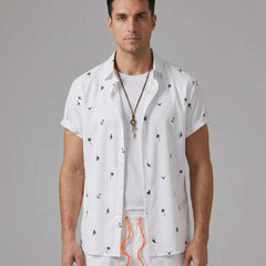 Three quarter view of man in white palm tree anchor sailboat print shirt and swim shorts
